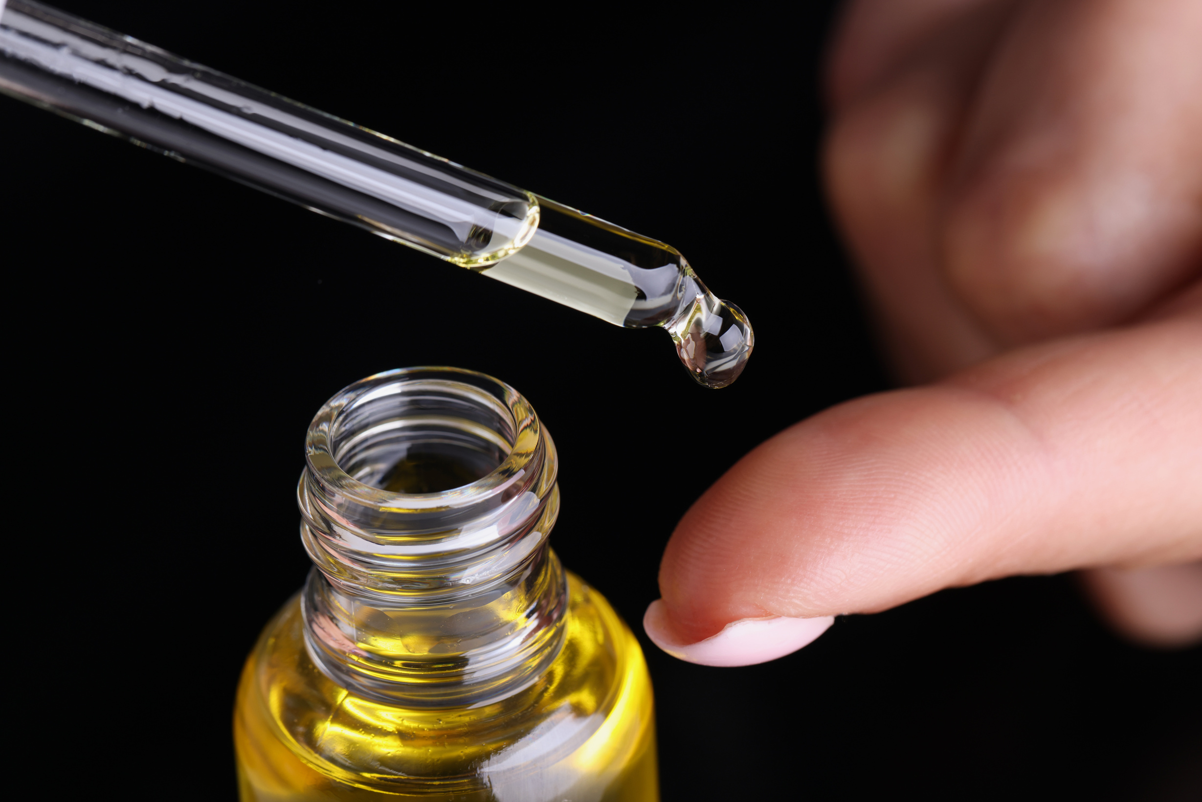 Person dripping drop of extract oil on finger with eyedropper